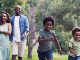 Happy, smiling and young family enjoying nature on a summer day outside. Excited children running while their parents walk in the park. A mother and father with a proud smile laughing at their kids